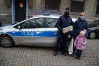 Wspólne zdjęcie na tle radiowozu policjanta, starszej kobiety i jej wnuczki