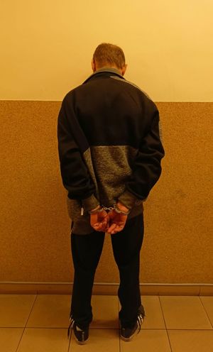 na zdjęciu zatrzymany mężczyzna stoi tyłem z kajdankami na ręku
